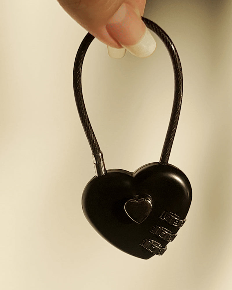 LoveBeats Black Heart Lock Charm, a chic travel accessory and luggage lock with a secure locking mechanism, held by two fingers.