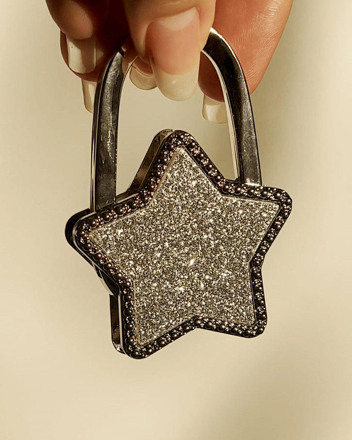 LoveBeats Crystal Star Purse Hook, a sparkling silver foldable bag holder with crystal pave design, held by two fingers.