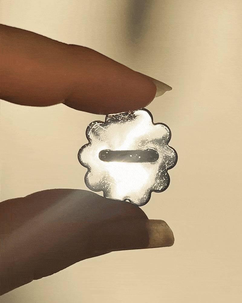 LoveBeats Floral Phone Charm Holder, a close-up of the elegant silver metal flower anchor point for phone cases, held between two fingers.