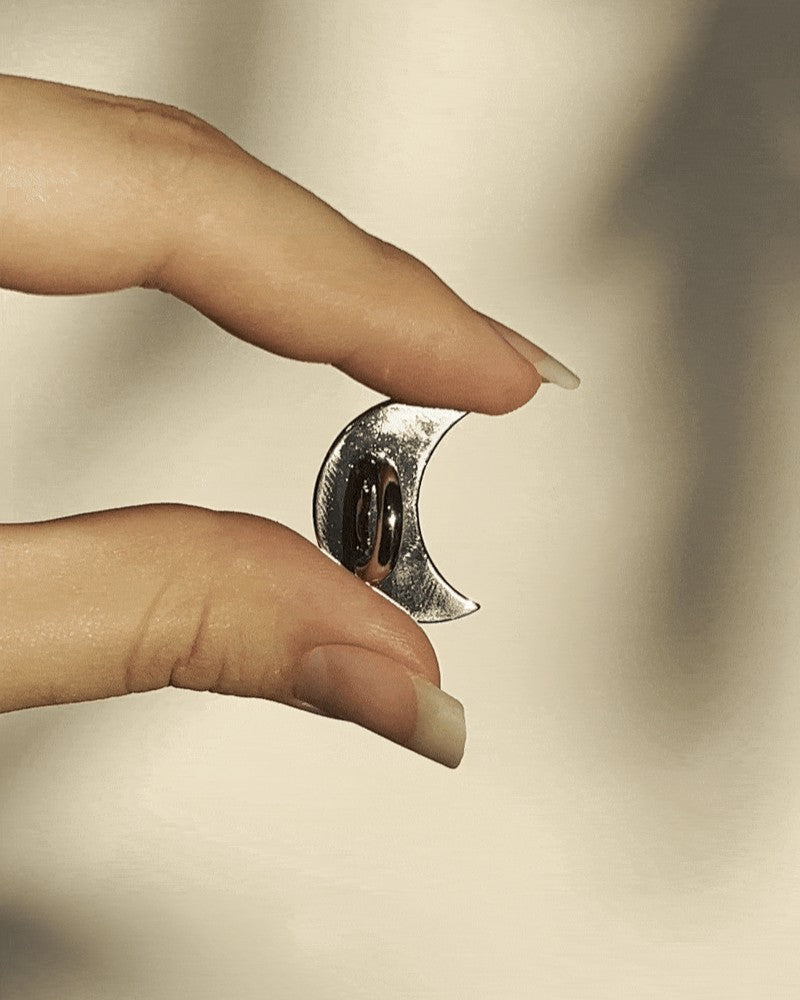 LoveBeats Moon Phone Charm Holder, a close-up of the minimalist silver crescent moon metal anchor point for phone cases, held by two fingers.