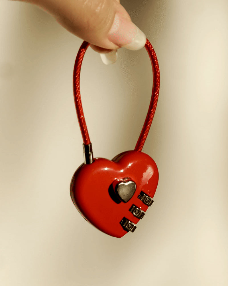 LoveBeats Red Heart Lock Charm, a close-up of the bright red travel padlock with a silver combination dial and durable wire loop, held by two fingers.
