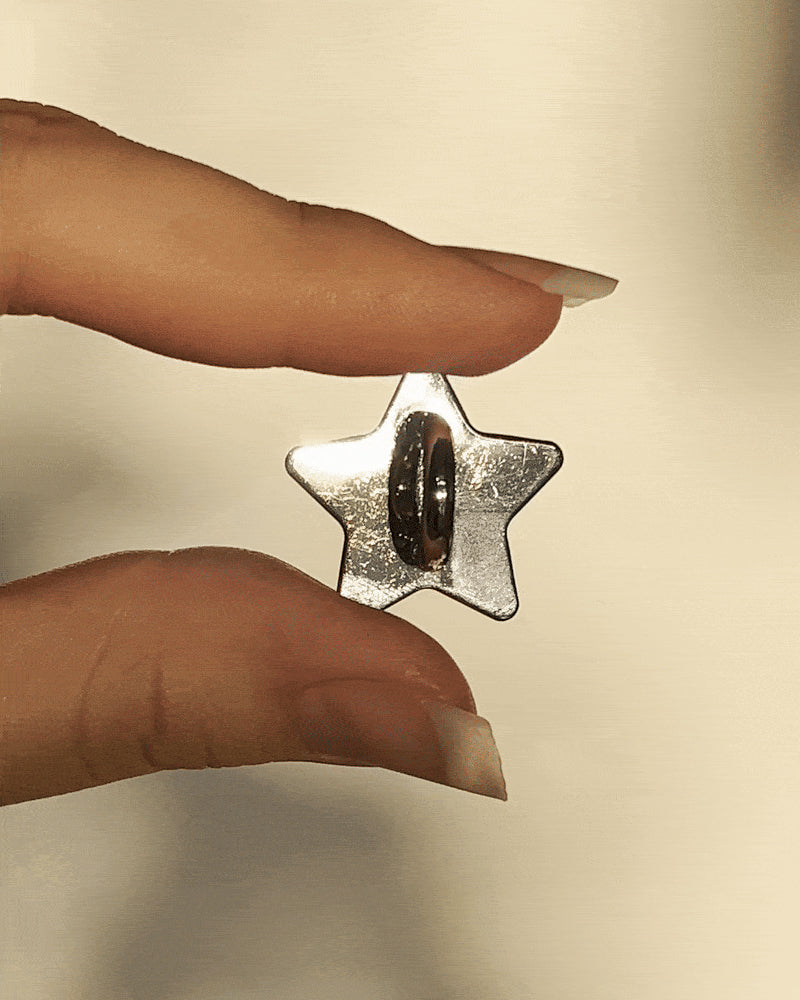 LoveBeats Star Phone Charm Holder, a close-up of the sleek silver metal star anchor point for phone cases, held between two fingers.