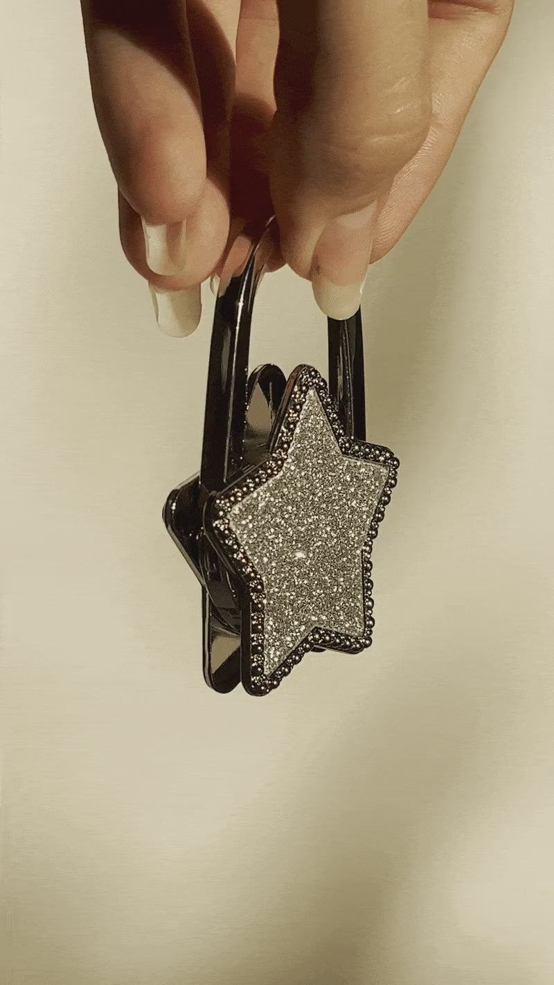 Close-up video of the Crystal Star Purse Hook by Love Beats, held between two fingers against a white background with warm sunset light.