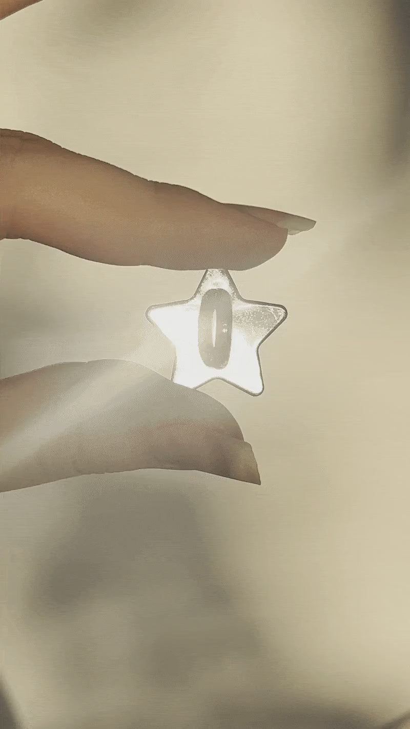 Close-up video of the Star Phone Charm Holder by Love BEATS, held between two fingers against a white background with warm sunset light.